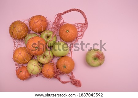 Red household mesh on a pink background with fruits. Apples and tangerines. For dessert.