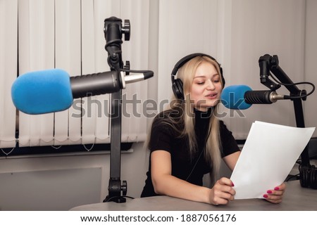 Young woman radio host in studio with headphones and microphone and talk news live. Cute female with clipboard hosting live show on station. Concept radio and Internet broadcasting for listeners