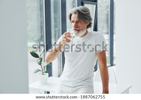 Drinks water. Senior stylish modern man with grey hair and beard indoors. Royalty-Free Stock Photo #1887062755