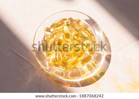 Cod liver fish oil capsules in glass bowl on pink background. Omega 3, Vitamin E supplements. Sunlight and shadows trendy shot. Healthy diet concept. Top view, close up, copy space