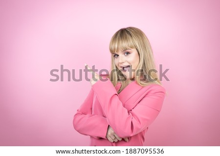 Young caucasian woman over isolated pink background surprised and pointing with hand and finger to the side