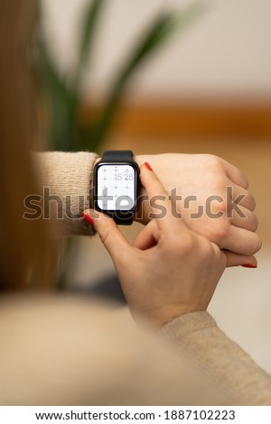 Smartwatch on girls hand with blank screen mock-up for your design at home office sitting on the couch near green plant with blurry background with free space for custom text