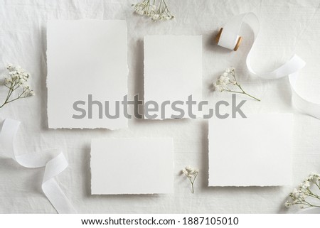Wedding invitation cards mockups top view. Flat lay blank paper cards, flowers, ribbon on white textile background. Minimal, elegant style.