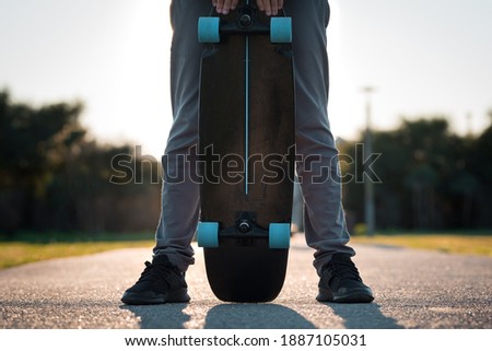 Man holding black longboard skateboard outdoors on sunset