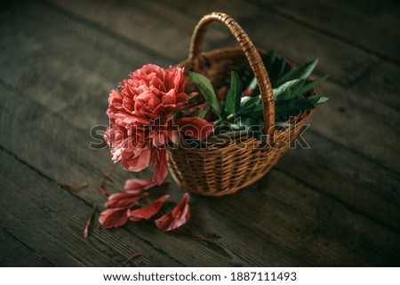 Wicker basket with red peony flower on wooden floor