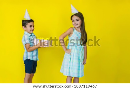 A little boy gives a gift to a girl on a bright yellow background.birthday of a little girl. the concept of celebration and fun.
