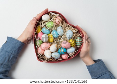 Heart shaped box with Easter eggs in children hands. White background. Top view.