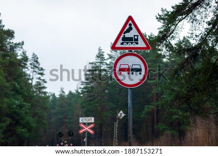 Traffic signs for railroad crossing, no overtaking and stop sign (Stop written in Russian) against forest trees on country road