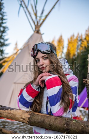 Portrait of Pretty Caucasian young woman Near Tipi or Wigwam in ski outfit and Winter Sports Mask on her Head. Portrait of cheerful blond woman at ski resort