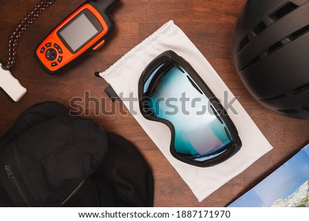 Overhead view of skiing gear and equipment including goggles, mittens, helmet, and GPS on a wooden background