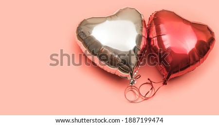 Two heart-shaped foil balloons on a pink background with place for text. Red and silver balloons on a light background.