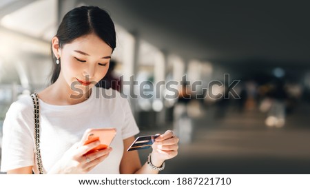 Business people shopping via online application media concept. Happy smile young adult asian woman consumer using creadit card and smartphone. City on day background with copy space. Royalty-Free Stock Photo #1887221710