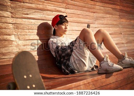 teenage asian skateboarder boy looking at cellphone while resting