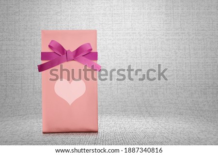 Pink gift box with red ribbon and heart with textured background