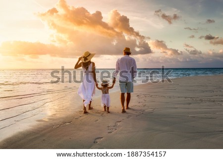 A elegant family in white summer clothing walks hand in hand down a tropical paradise beach during sunset tme and enjoys their vacation time Royalty-Free Stock Photo #1887354157