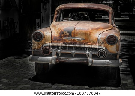 front of a parking  antique car with chrome bumper and grill, rusty fenders and hood and broken head lamps Royalty-Free Stock Photo #1887378847