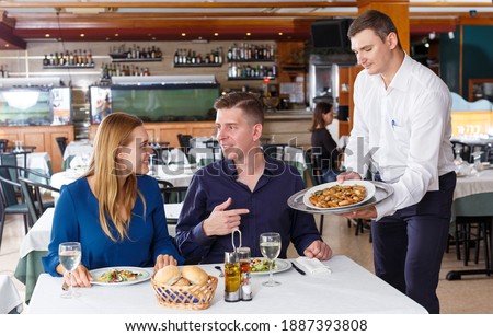 Friendly waiter serving tasty dishes - order of couple having dinner at restaurant