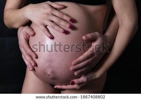 Scene on black background of belly in advanced state of gestation, young woman 9 months pregnant with her hands and those of her partner touching gently the belly.