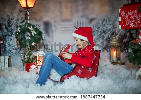 Cute child, school boy, opening present for christmas, decoration around him, outdoor shot, outdoor snow shot