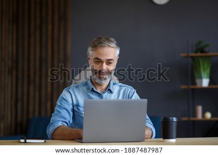 Grey-haired senior man working in home office with laptop. Business portrait of handsome manager sitting at workplace. Studying online, online courses. Business concept.
