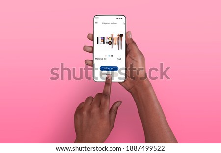 Female Shopping Concept. Above top overhead view of black woman browsing online make up store on her smart phone, isolated on pink background, touching screen. Customer ordering via internet Royalty-Free Stock Photo #1887499522