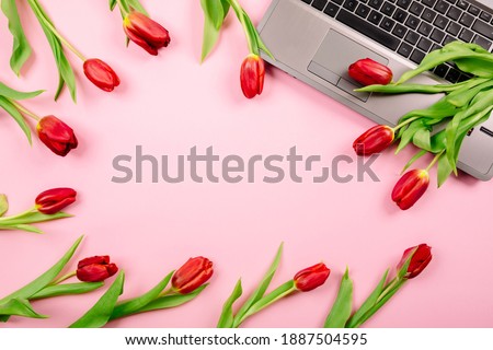 Red tulips in shape of frame on pink paper background with a laptop on desktop. Template for advertising or blog visualization with copy space, text place. Business card. Holiday certificate. Banner.