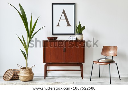 Stylish interior design of living room with wooden retro commode, chair, tropical plant in rattan basket, decoration and elegant personal accessories. Mock up poster frame on the white wall. Template