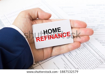A man's hand is on the financial tables holding a business card with the inscription Home Refinance. Business concept photo