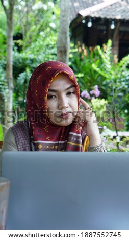 Muslim woman in hijab sitting at a table with a laptop in a cafe. Modern casual Muslim fashion