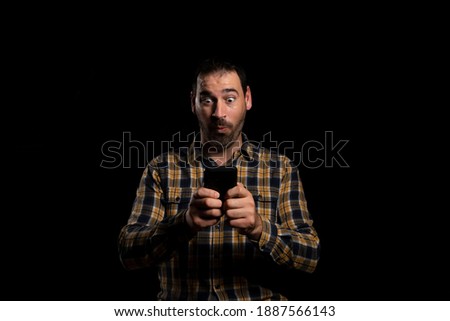 Attractive bearded man in a yellow plaid shirt using mobile isolated on black background. Technology concept
