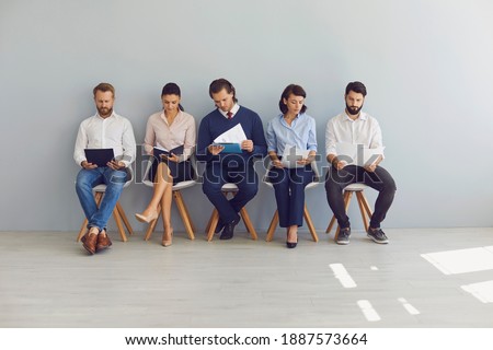 Group of young people job seekers or applicants sitting on chairs in row with resumes and waiting in line for interview invitation in office of modern company. Office career seekers concept Royalty-Free Stock Photo #1887573664