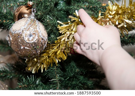 Woman adding tinsel to a Christmas tree after adding tan and gold decorative globes
