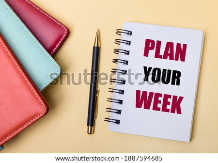 Multi-colored diaries lie on a beige background next to a pen and a notebook with the words PLAN YOUR WEEK. Flat lay.