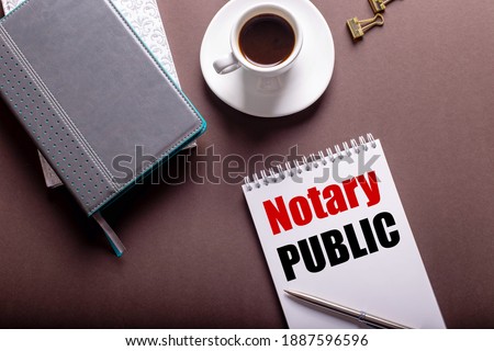 On a brown background, diaries, a white cup of coffee and a notebook with NOTARY PUBLIC