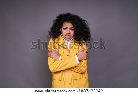 Photo of a frozen, twisted face, dark-skinned girl with curly black hair in a white sweater and a yellow raincoat hugging her shoulders, the girl froze. Copy space.