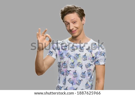 Handsome teen boy making ok gesture with fingers. Funny teenage boy showing okay against gray background.