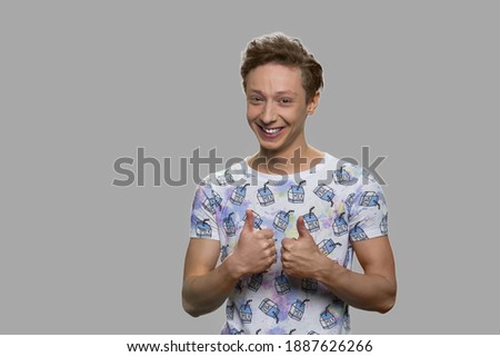 Happy teenage boy showing thumbs up. Cute smiling teenage boy looking at camera against gray background.