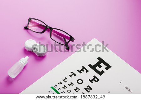 Ophthalmologist accessories glasses, lenses and vitamins with a test target for vision correction on a pink background. Treating vision problems. Top view, free space