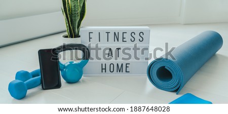 Fitness at home lightbox sign in living room for online workout on phone app training indoors with dumbbell weights and resistance bands on yoga mat banner background.