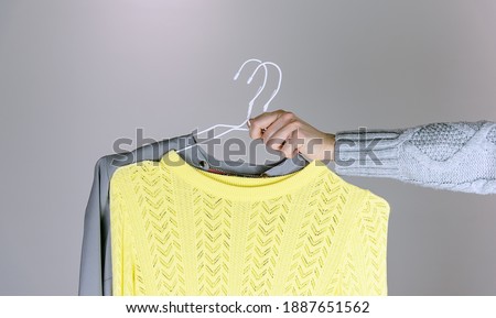 Female hands holding two blouses in trendy colors. Colors of the year 2021 Ultimate Gray and Illuminating. 