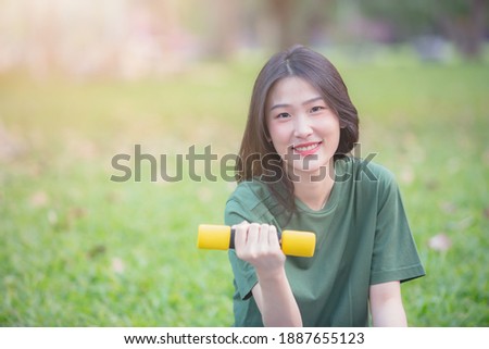 Young beautiful Asian woman holding dumbbell to workout in the park