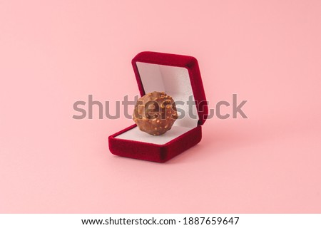 Creative  minimal style Valentines day composition with red engagement ring box with chocolate hazelnut praline on pastel pink backgroud. Royalty-Free Stock Photo #1887659647
