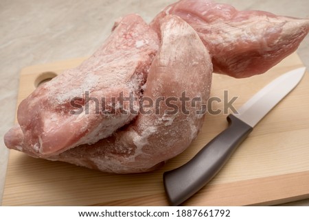 Frozen meat, raw at home on the table. On a wooden board. And a cutting knife. For cooking food.