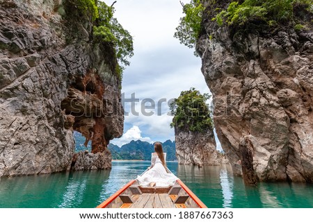 Back View of Young Female Tourist in Dress and Hat at Longtail Boat near Famous Three rocks with Limestone Cliffs at Cheow Lan Lake. Travel Woman Sitting on Boat in Khao Sok National Park in Thailand Royalty-Free Stock Photo #1887667363