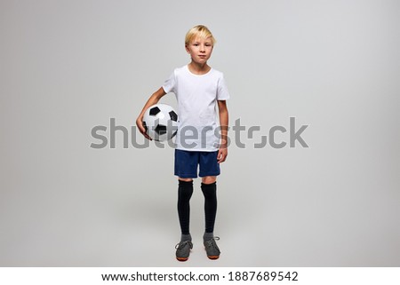 football player with ball isolated in studio, posing at camera, wearing football uniform, white t-shirt. sport, soccer concept