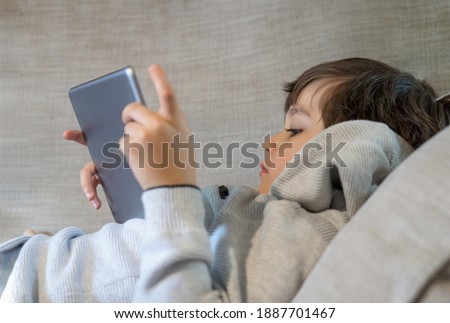Cropped shot kid lying on sofa watching cartoons on tablet,6-7 year old boy playing game on touch pad, Cute Kid having fun and relaxing on his own in living room, New normal lifestyle 