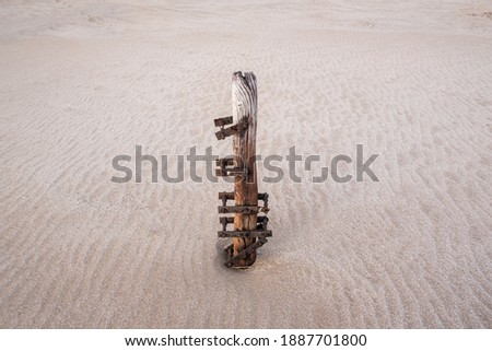 Old wooden fence post with rusty iron grips, buried in sand