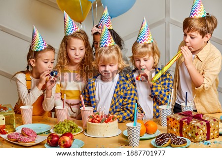 happy birthday party. children in party caps celebrating birthday at home in light room, kids with delicious food behind table