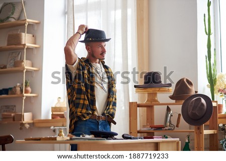 designer jeweler at work place, young man engaged in creative work consisted of repairing rare and old things, he stands in contemplation, wearing hat