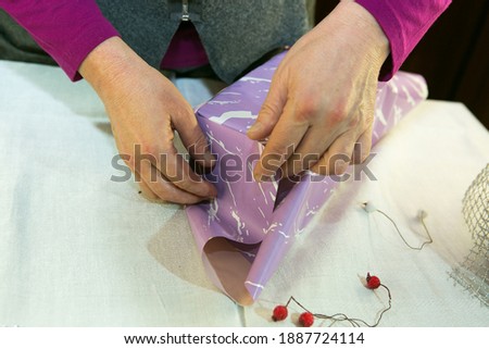 The process of wrapping gifts for the holiday. Women's hands work with scissors, an adhesive device, ornaments. Home shooting in quarantine conditions.